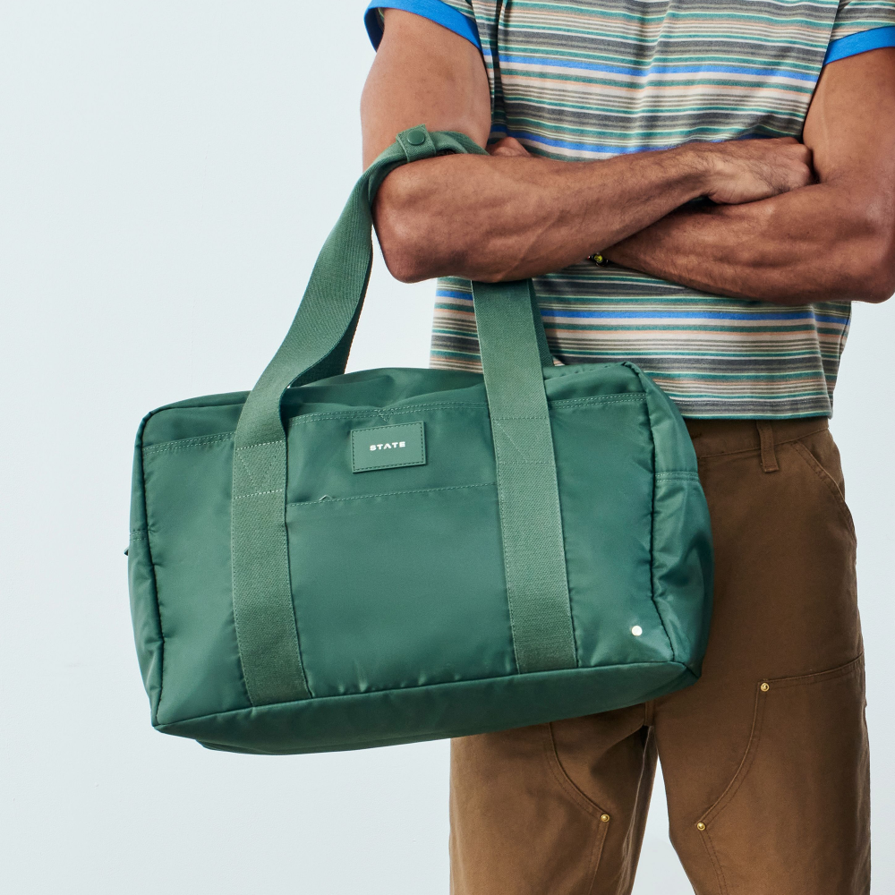 Person holding a green duffel bag against a light gray background