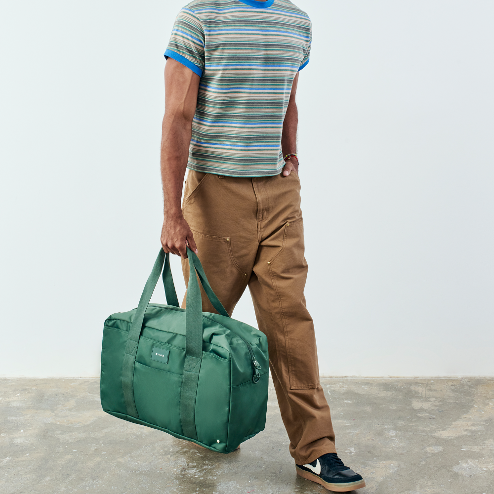 Person holding a green duffel bag against a plain background