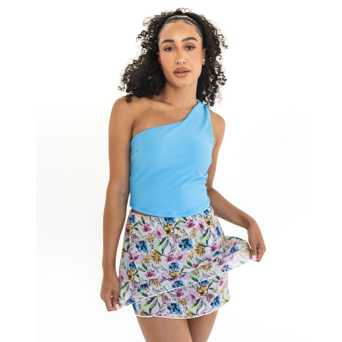 Woman wearing a blue one-shoulder top and floral skirt on a white background