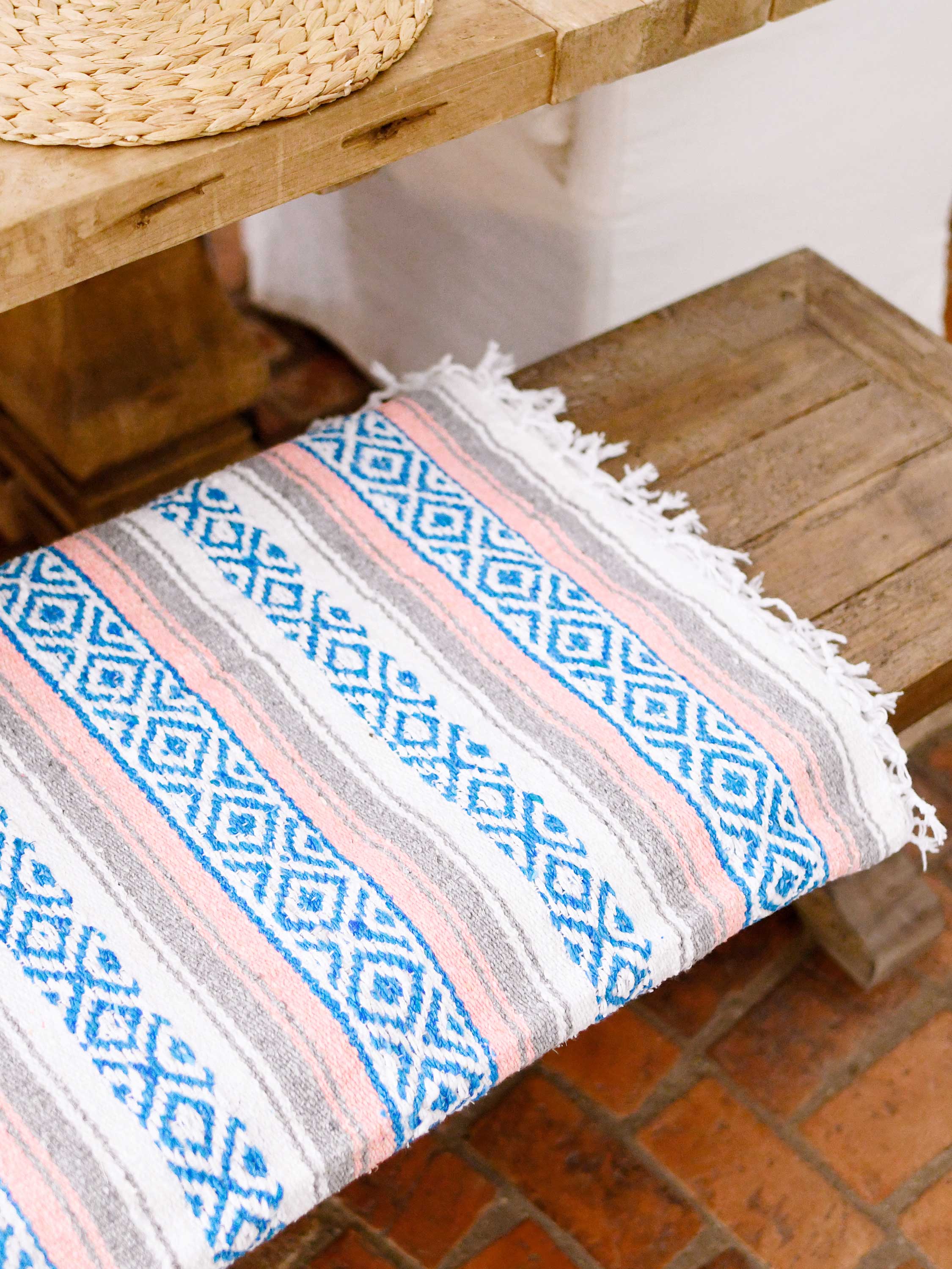 Patterned fabric on a wooden stool with a wicker chair in the background.