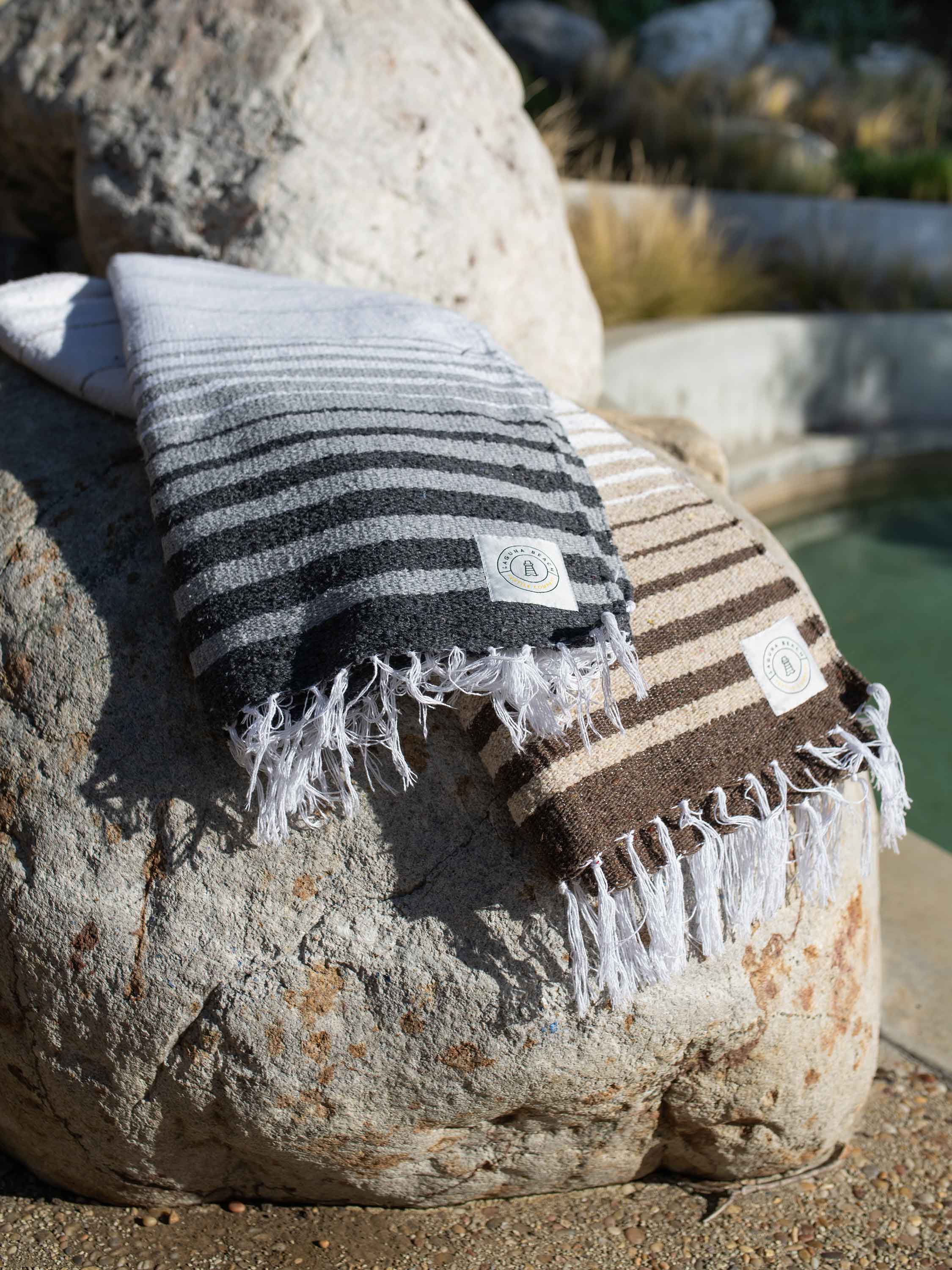 Two striped towels, one black and white and one brown and beige, draped over a rock by a pool.