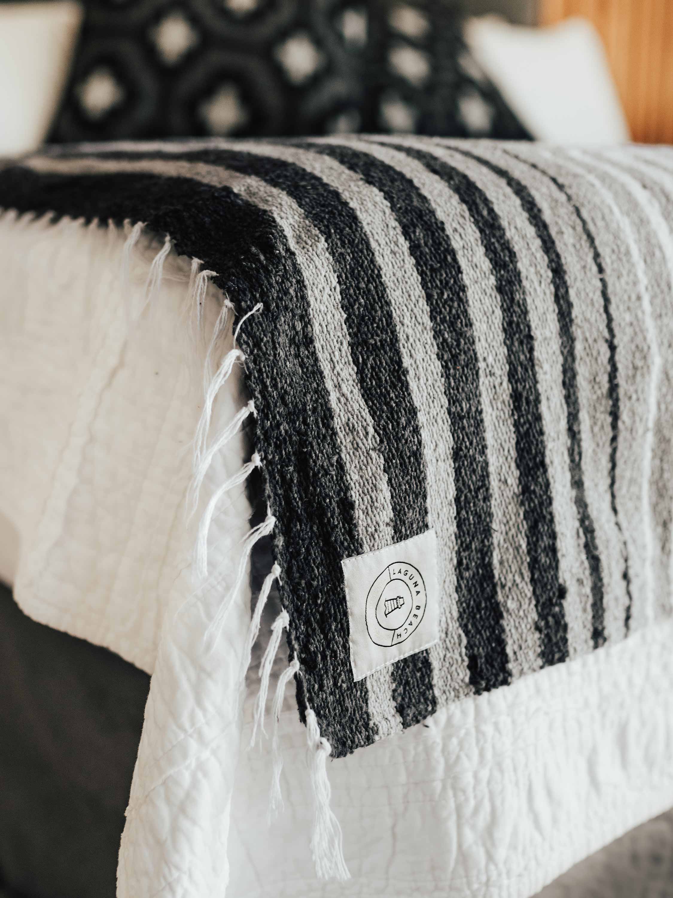 Black and white striped blanket draped over a bed with a visible brand label.