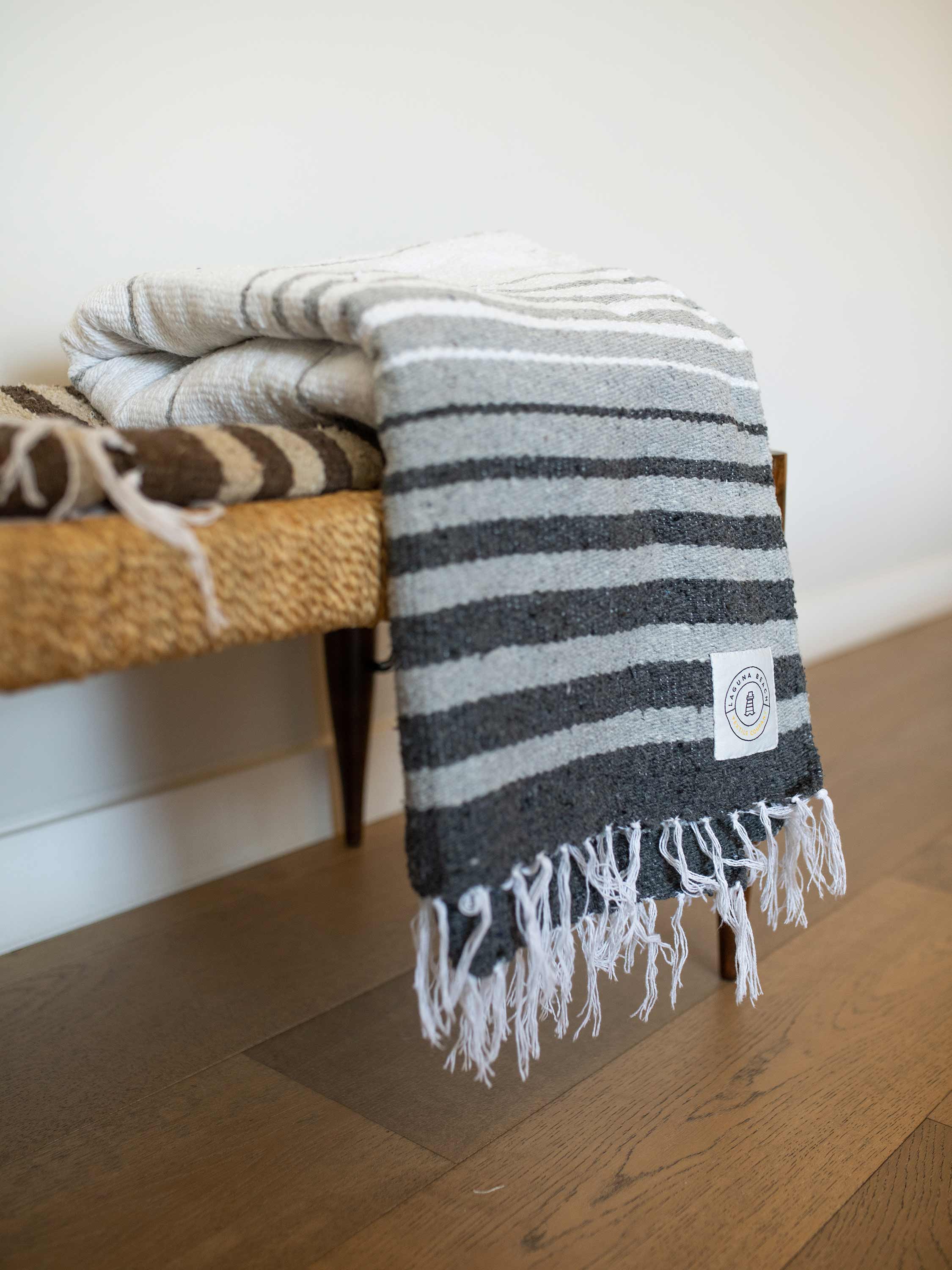 Striped blanket with a brand logo draped over a wooden bench on a wooden floor.