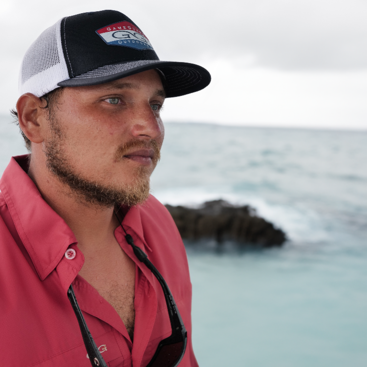 Man wearing a red shirt and black and white cap with ocean in the background