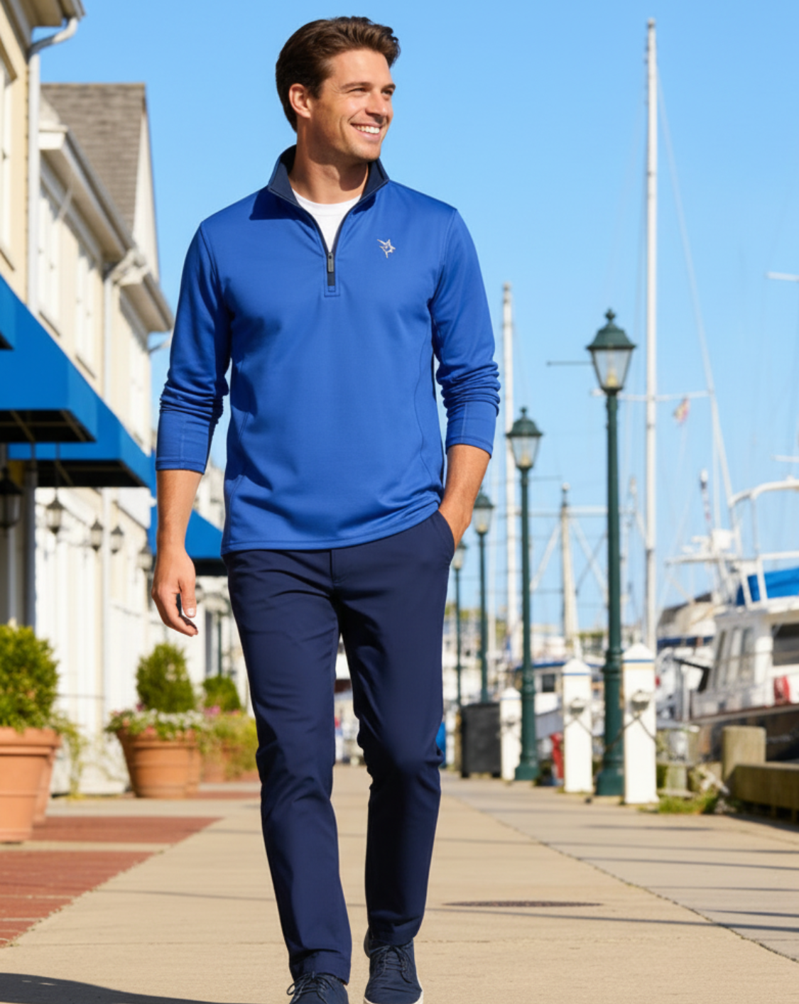 Man in a blue pullover and navy pants walking along a waterfront promenade.