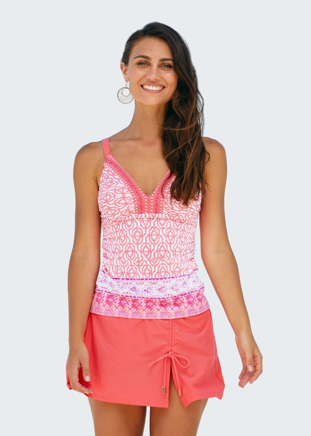 Woman wearing a pink patterned top and coral skirt on a beach
