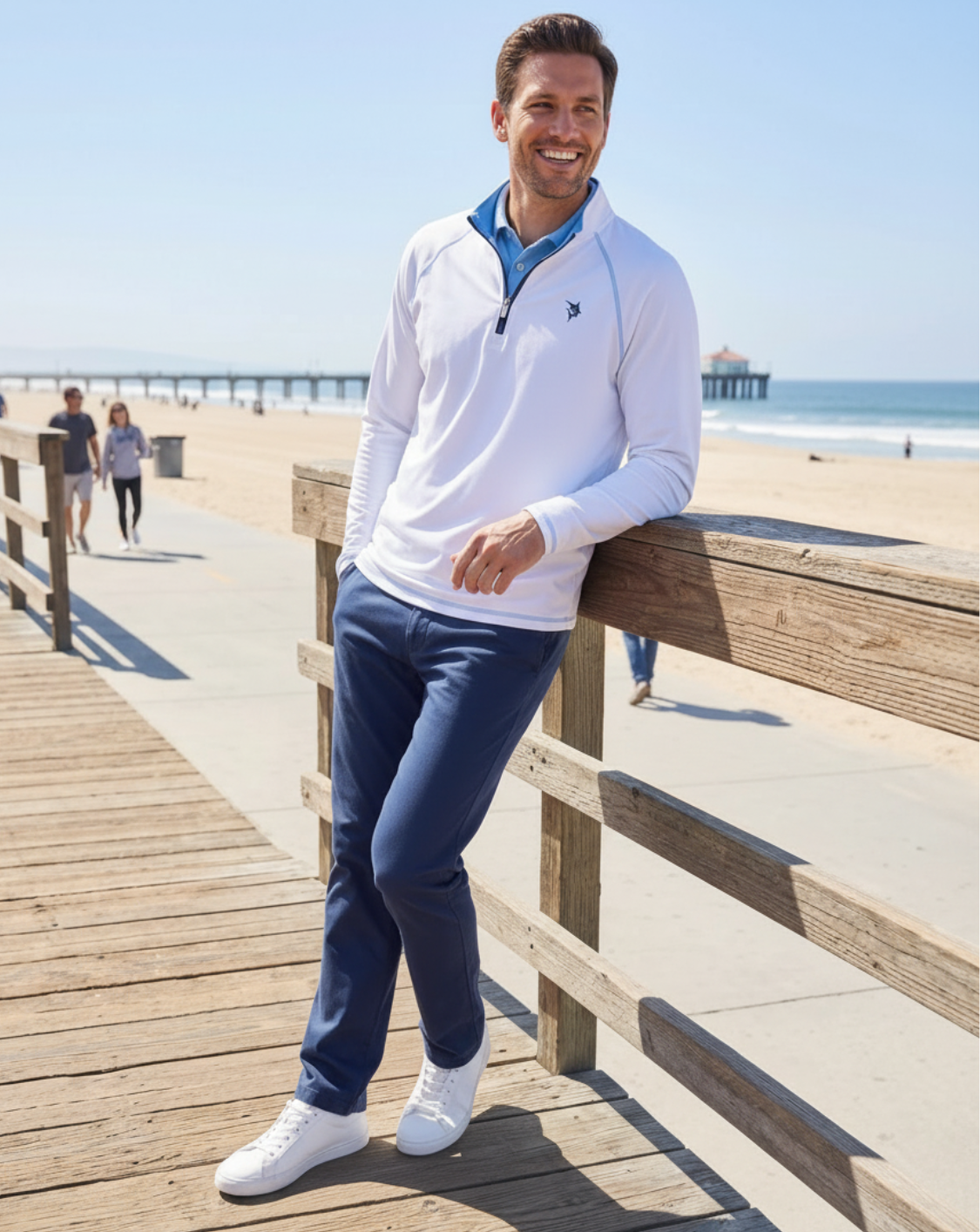 Man standing on a wooden boardwalk by the beach wearing a white and blue outfit.