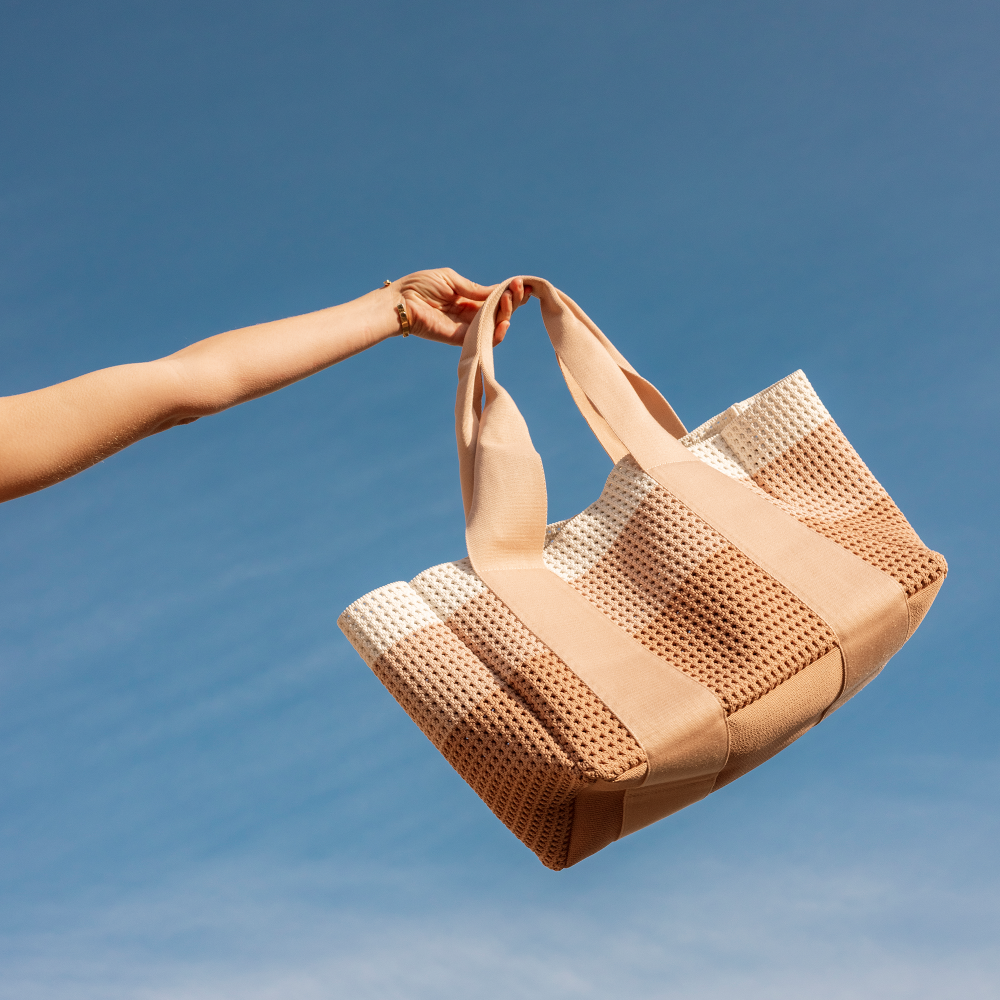 Beige woven handbag held against a clear blue sky