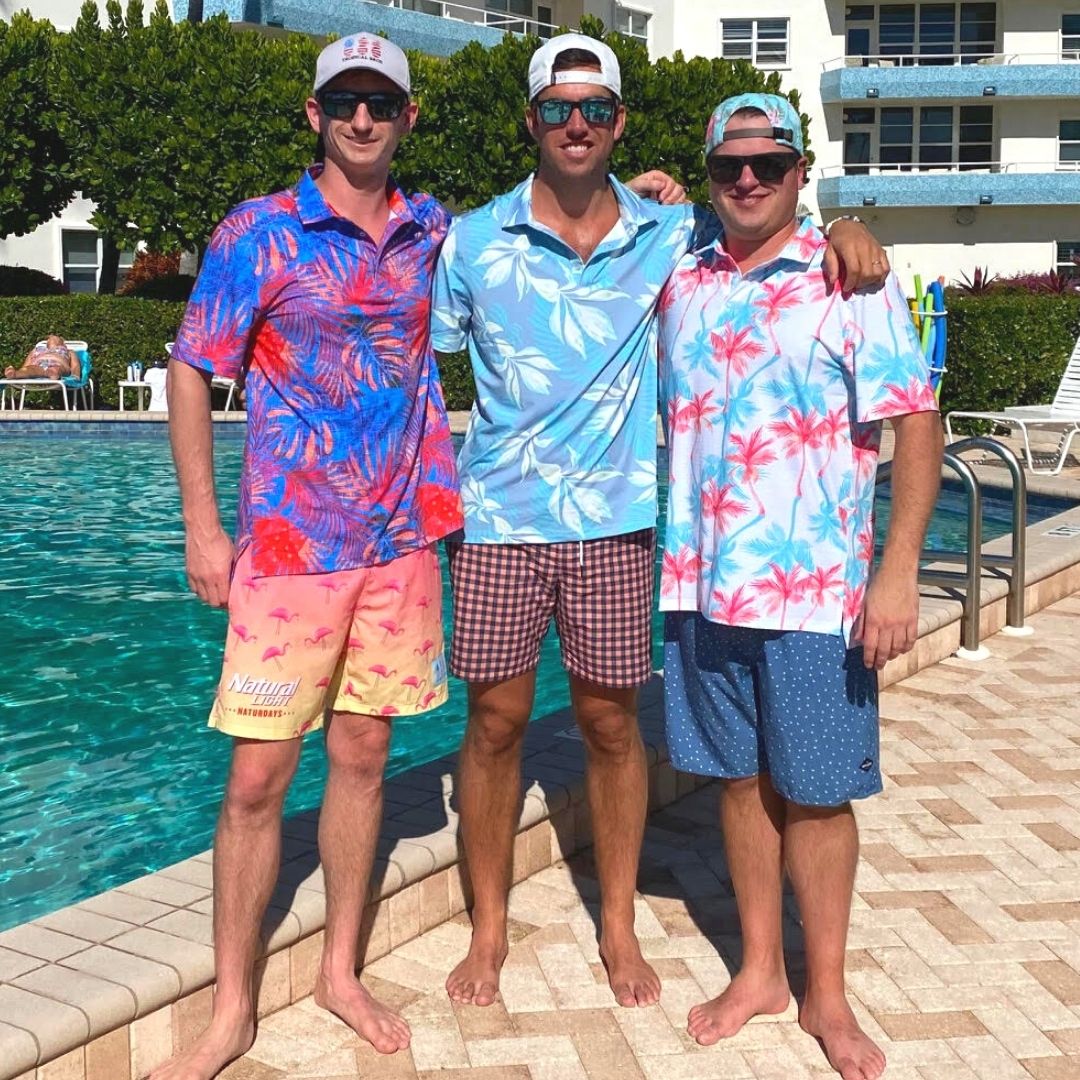 Three men in colorful swimwear and hats posing by a pool.