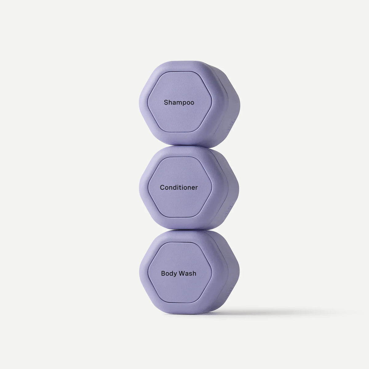 Three small hexagonal lavender shampoo, conditioner, and body wash containers stacked vertically on a clean off-white background.