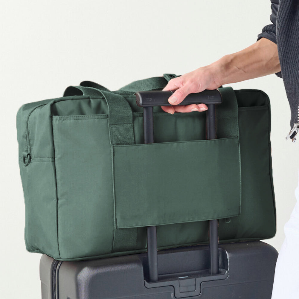 Green duffel bag being held on top of a suitcase with a neutral background