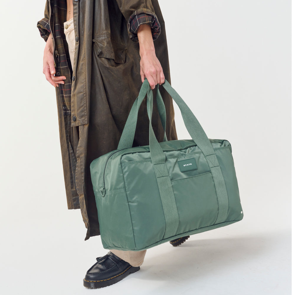 Person holding a green duffel bag against a white background