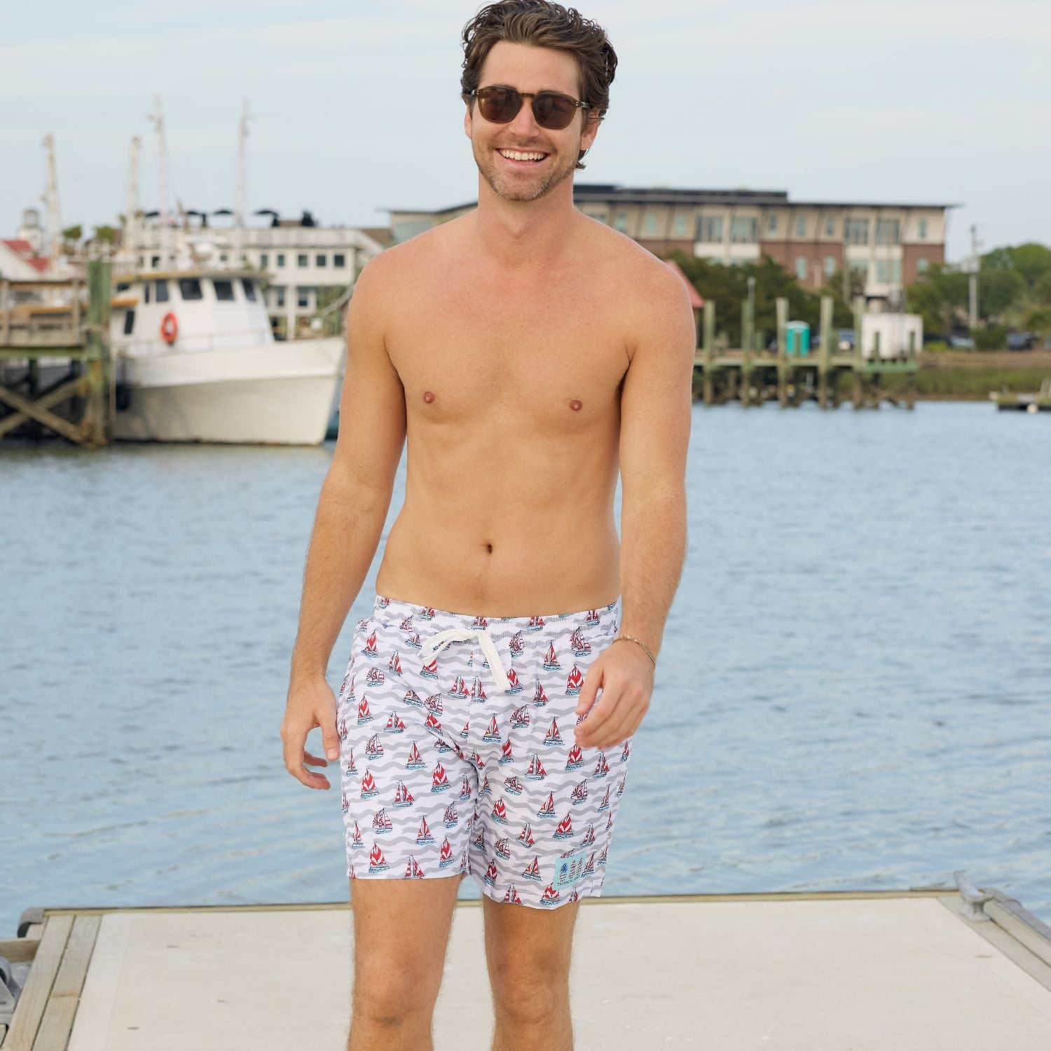 Man wearing swim shorts with a boat pattern by a waterfront