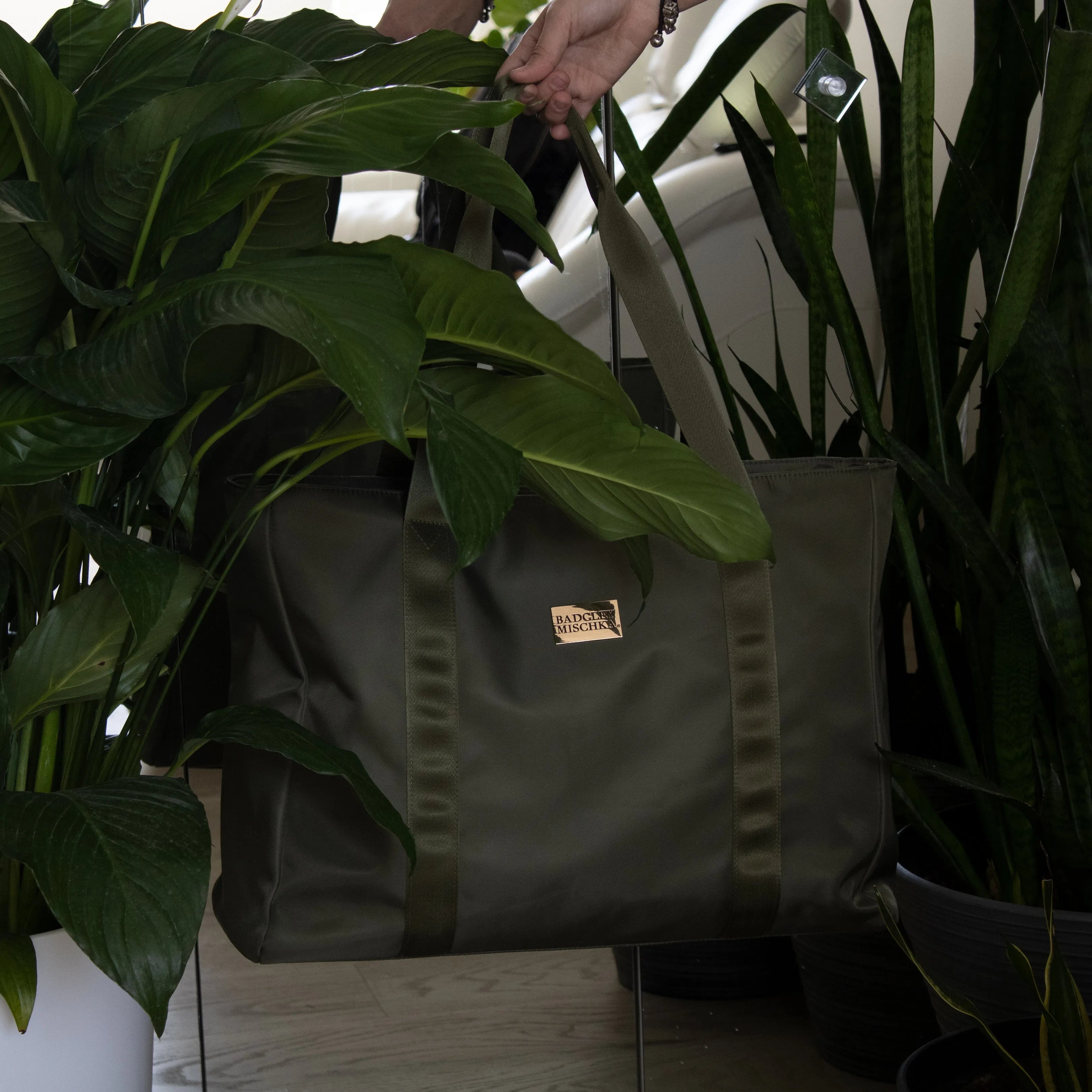 Gray bag with a brand logo held by a person among potted plants.