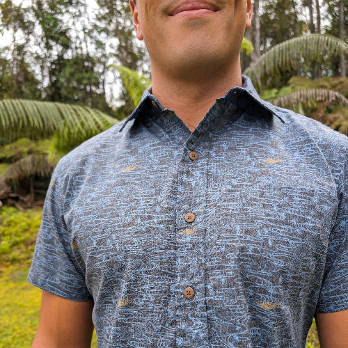 Man wearing a patterned blue shirt outdoors with greenery in the background