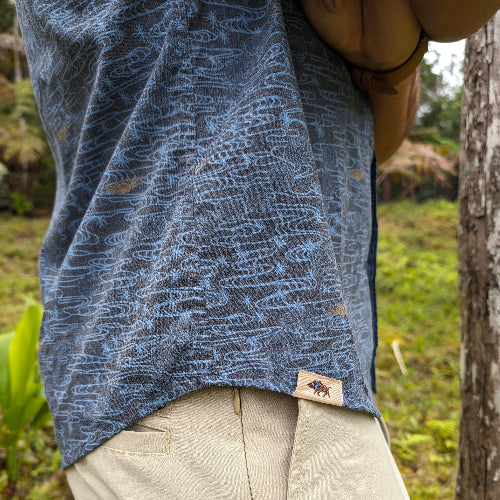 Person wearing a blue patterned shirt with a brand logo in a natural setting