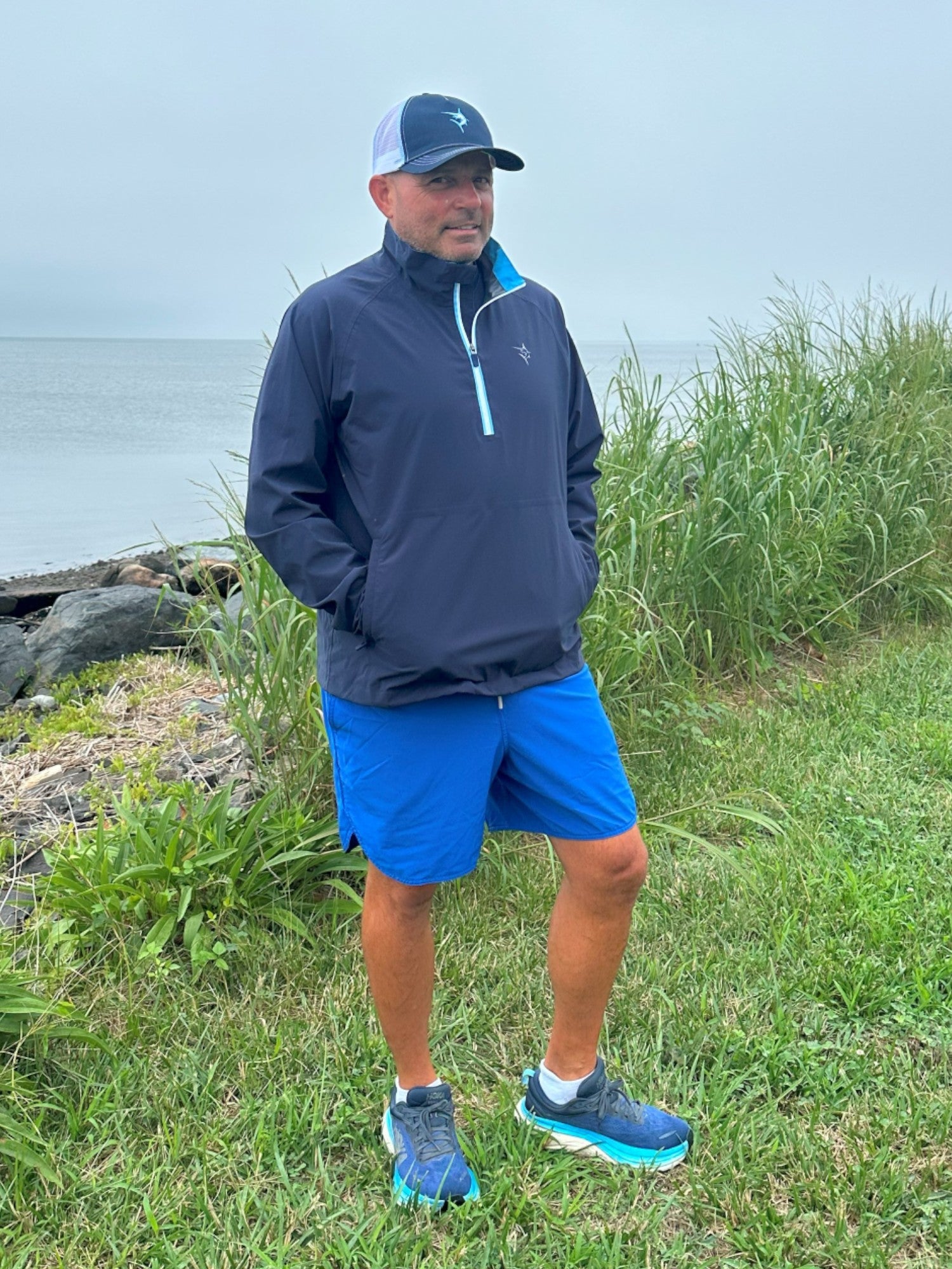 Man in athletic wear standing by a body of water with grass and rocks in the background