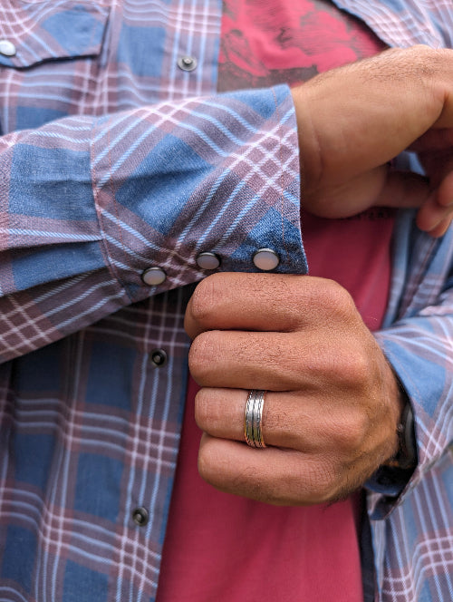 Close-up of a person wearing a plaid shirt with rolled-up sleeves and a ring on their finger.