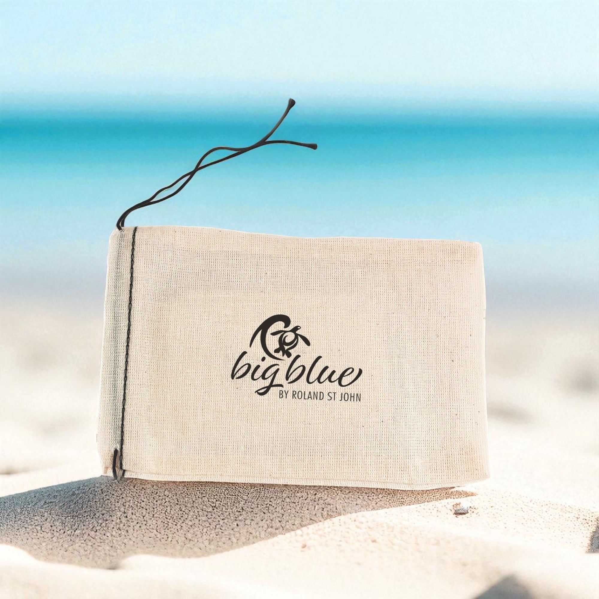 Beige pouch with 'bigblue' logo on sand and ocean background