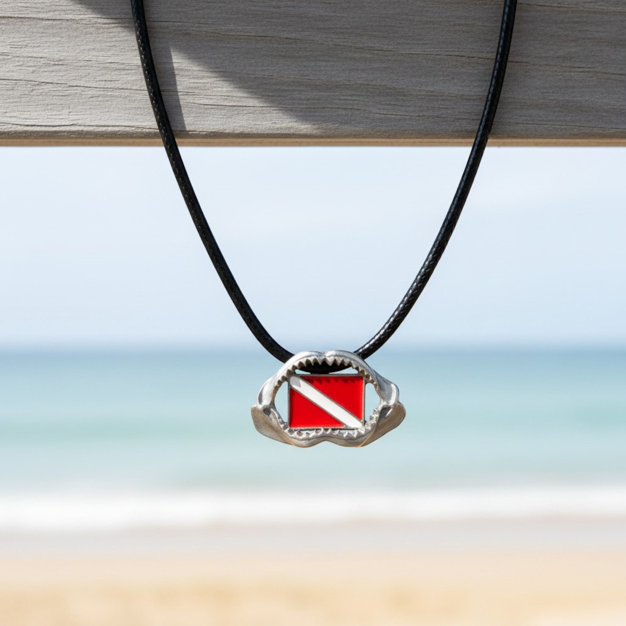 Necklace with a red and white diving flag pendant on a blurred beach background