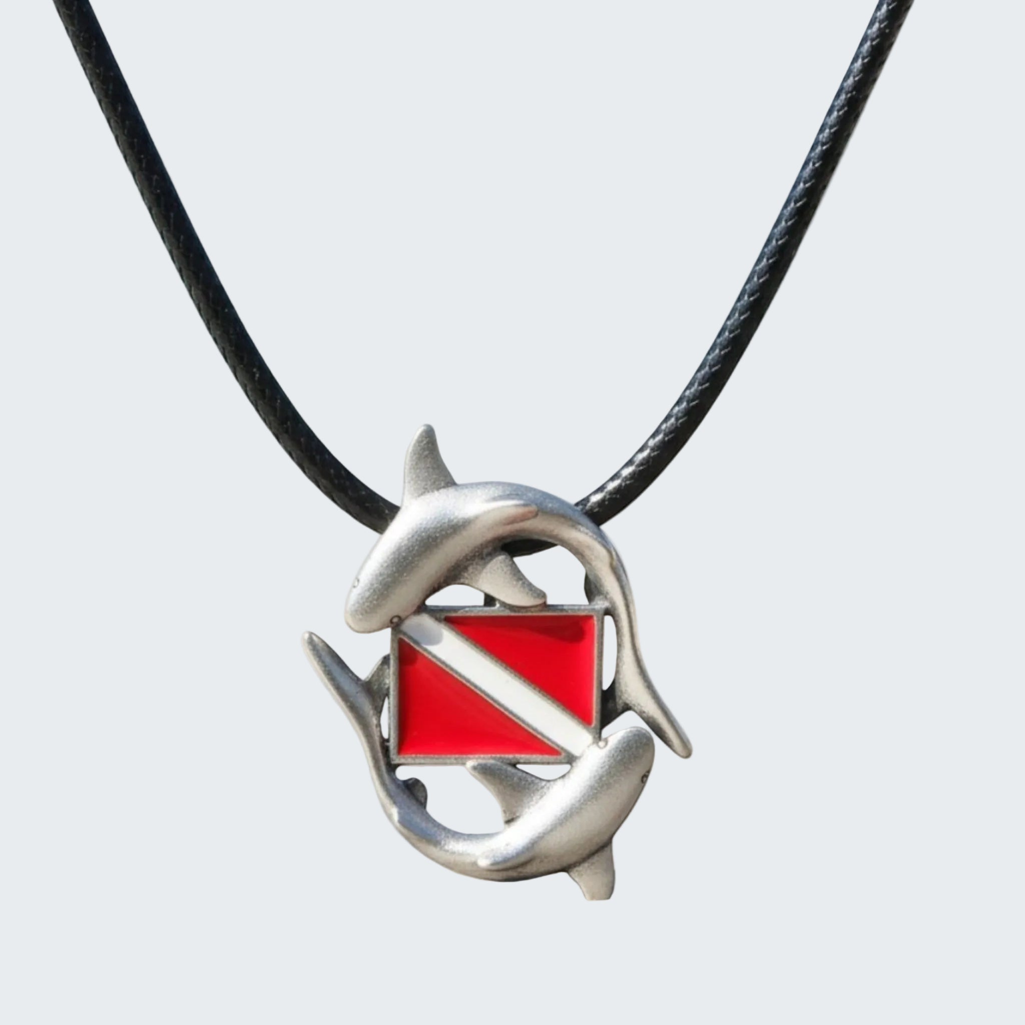 Dolphin pendant with a red square and black cord against a blurred beach background