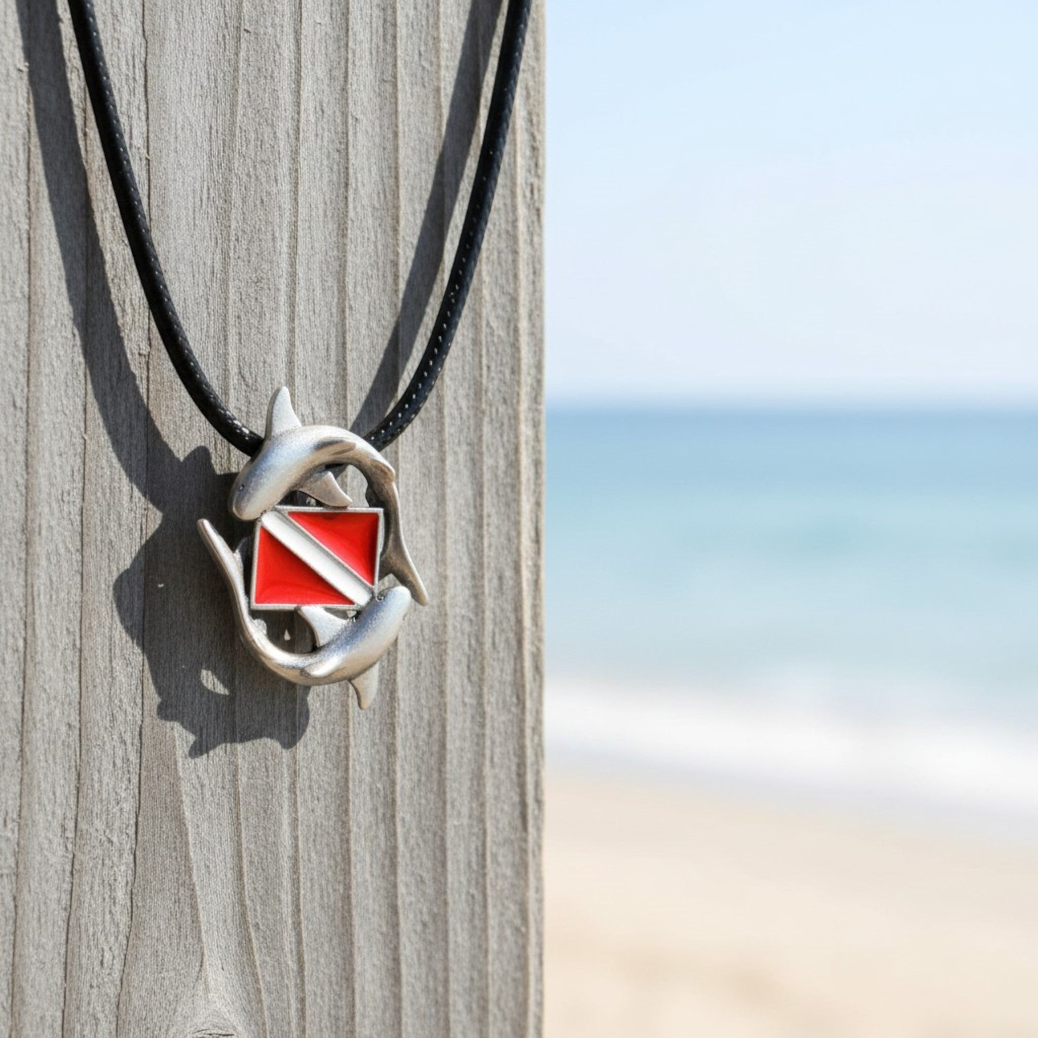 Necklace with a shark tooth and red and white flag pendant on a wooden post with a beach background