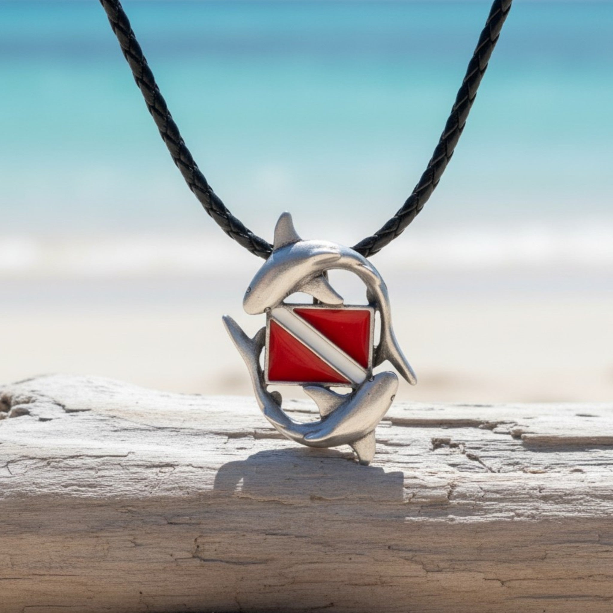 Diving pendant with red and white design on a black cord, placed on driftwood with a beach background.