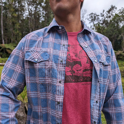 Person wearing a blue plaid shirt over a red graphic t-shirt with a forest background