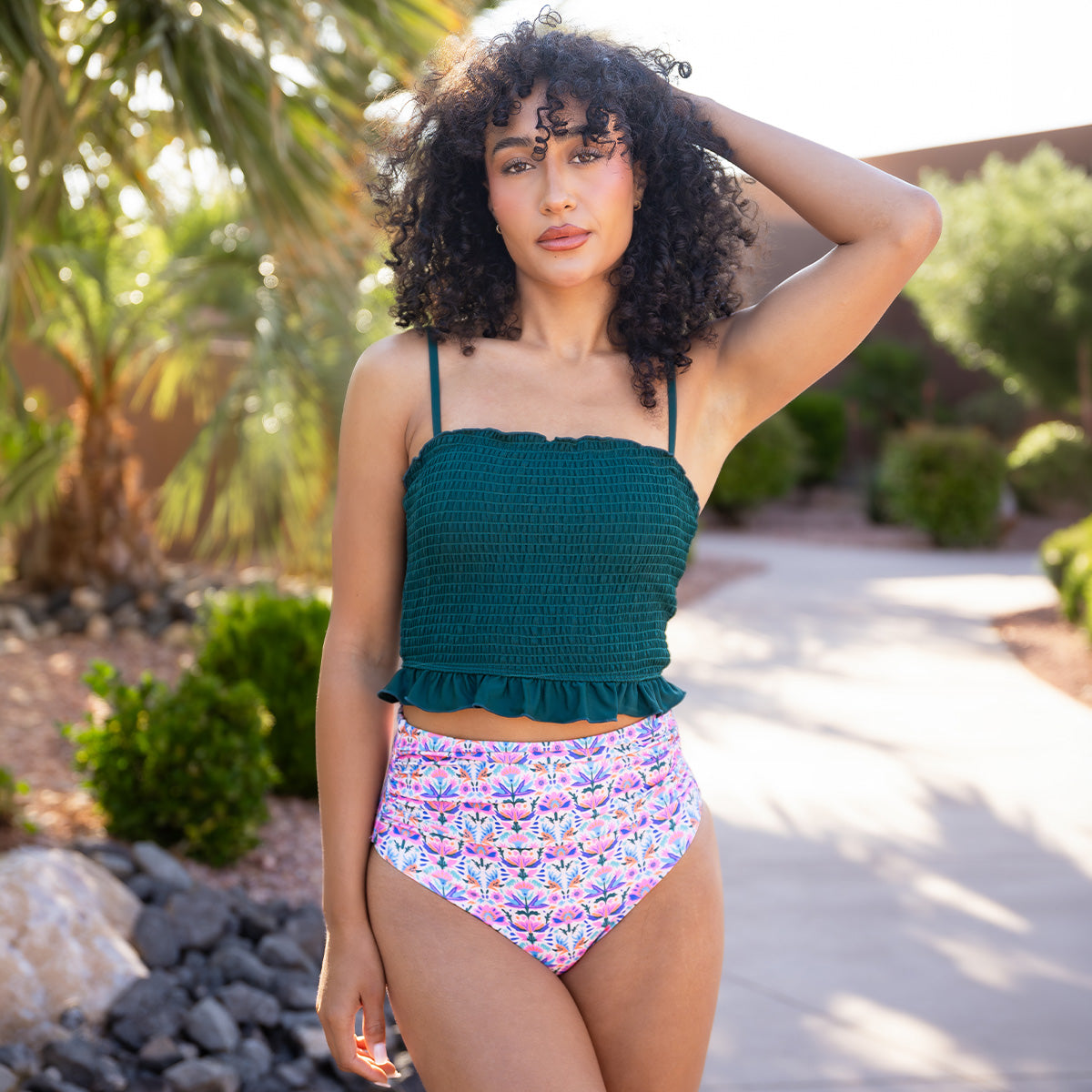 Woman wearing a green top and colorful high-waisted bikini bottom outdoors.