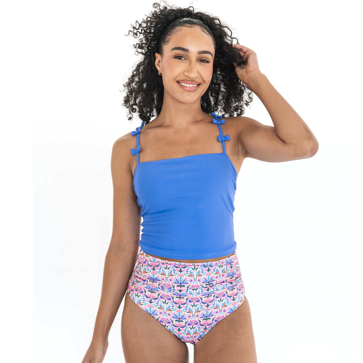 Woman wearing a blue tank top and floral high-waisted bikini bottom on a white background