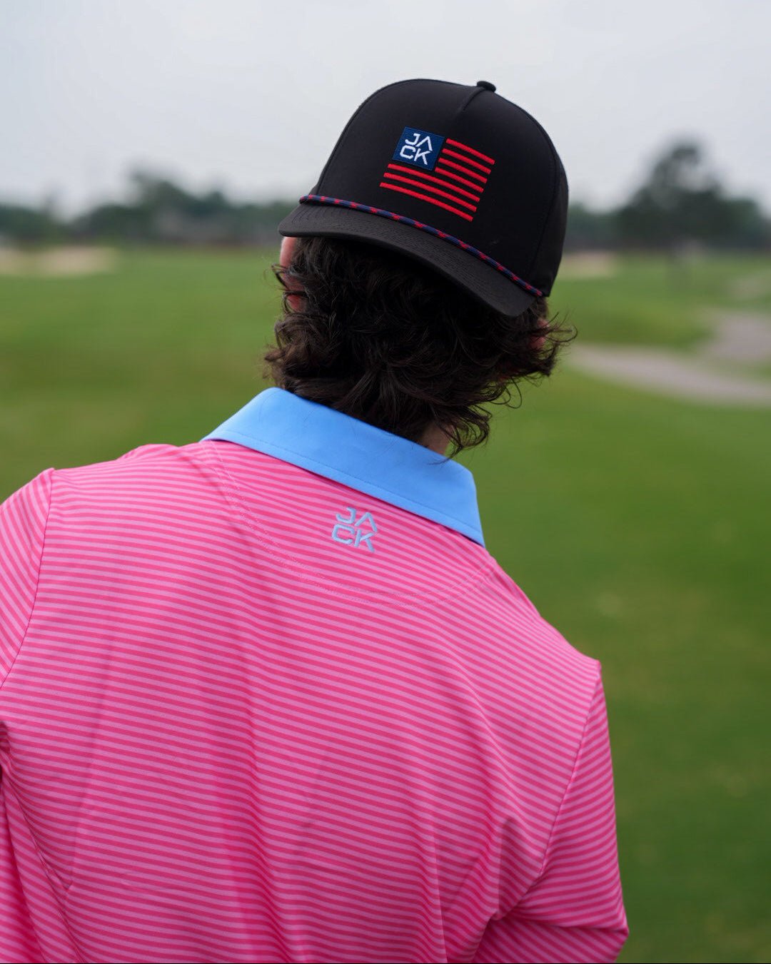 Person wearing a pink shirt and black cap with a logo on a golf course