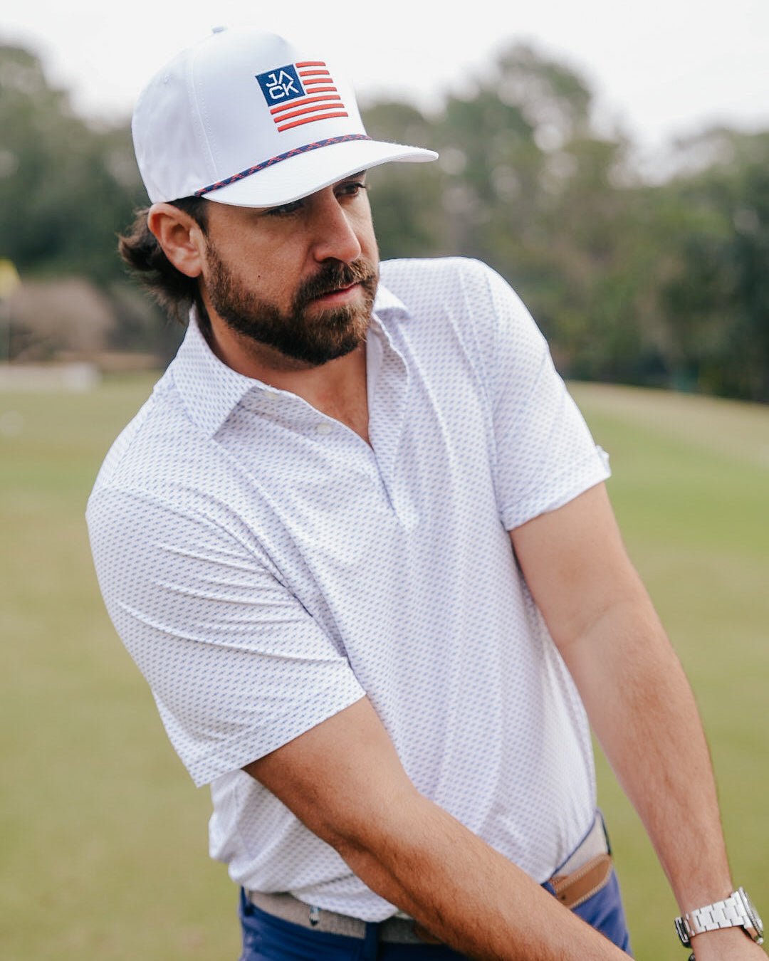 Man wearing a white cap with an American flag design on a golf course