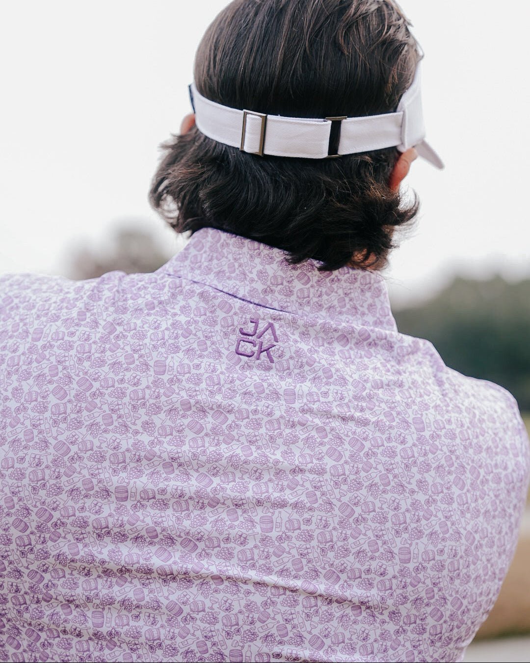 Person wearing a white visor and patterned shirt with a logo, outdoors.