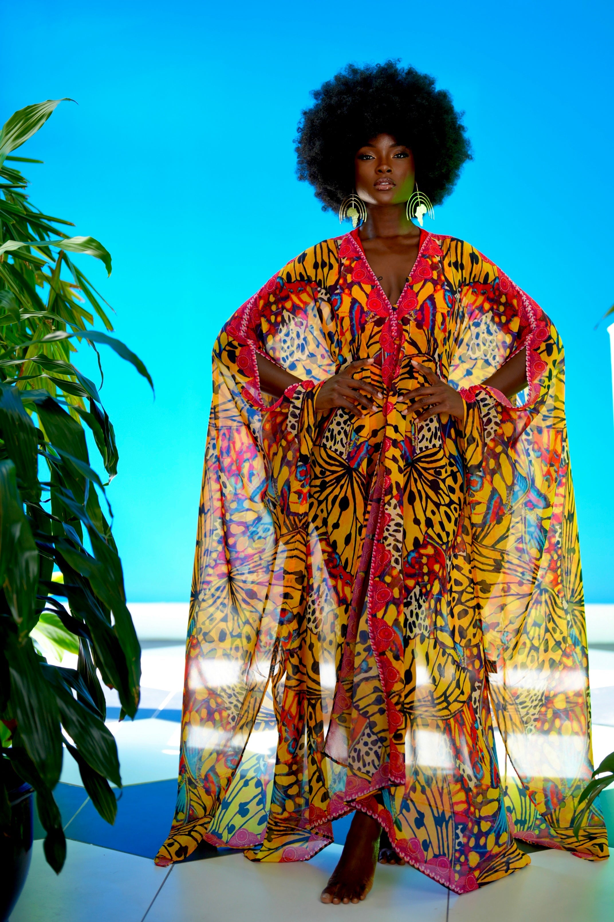 Woman wearing a colorful patterned dress with a blue sky and plant in the background