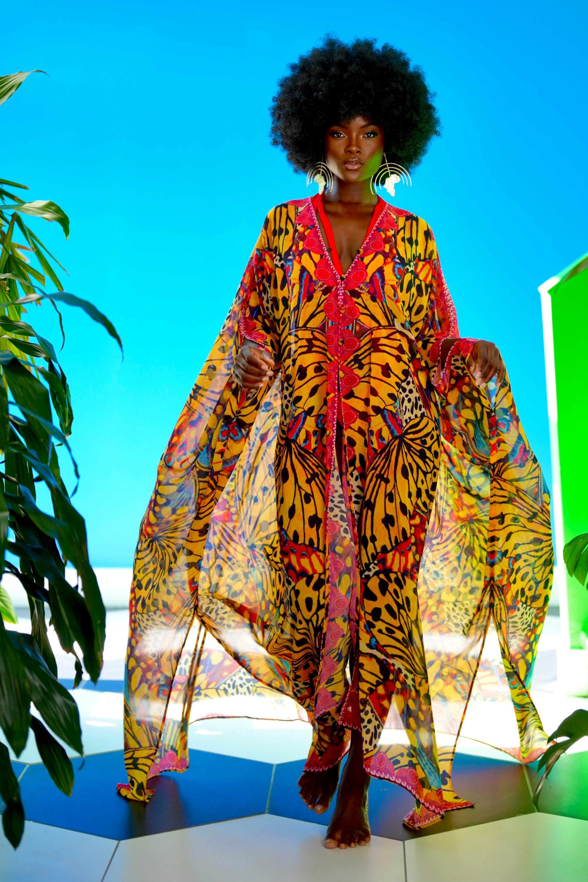 Woman wearing a colorful patterned outfit with a bright blue sky and green plants in the background
