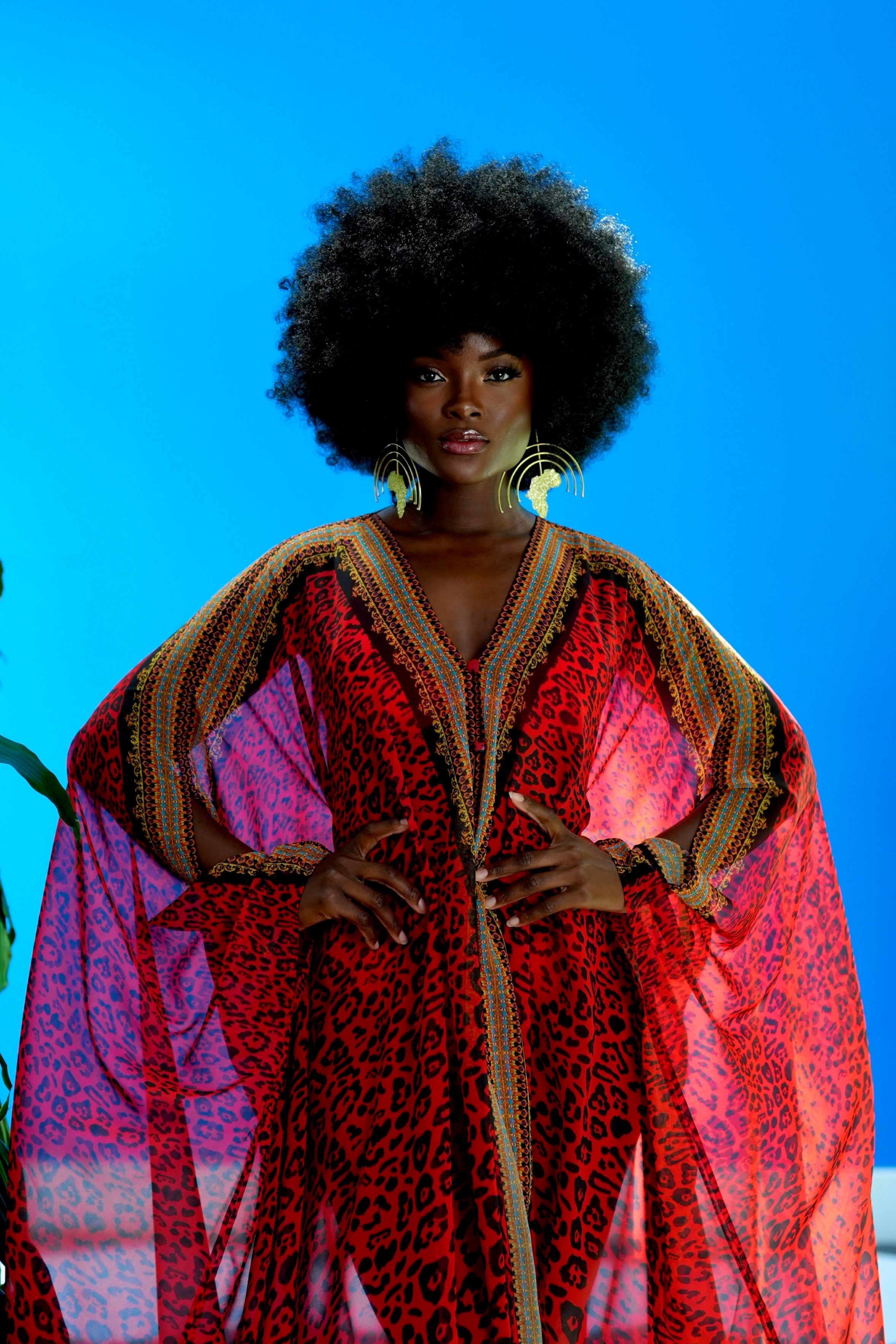 Woman wearing a vibrant red and pink patterned dress against a blue background