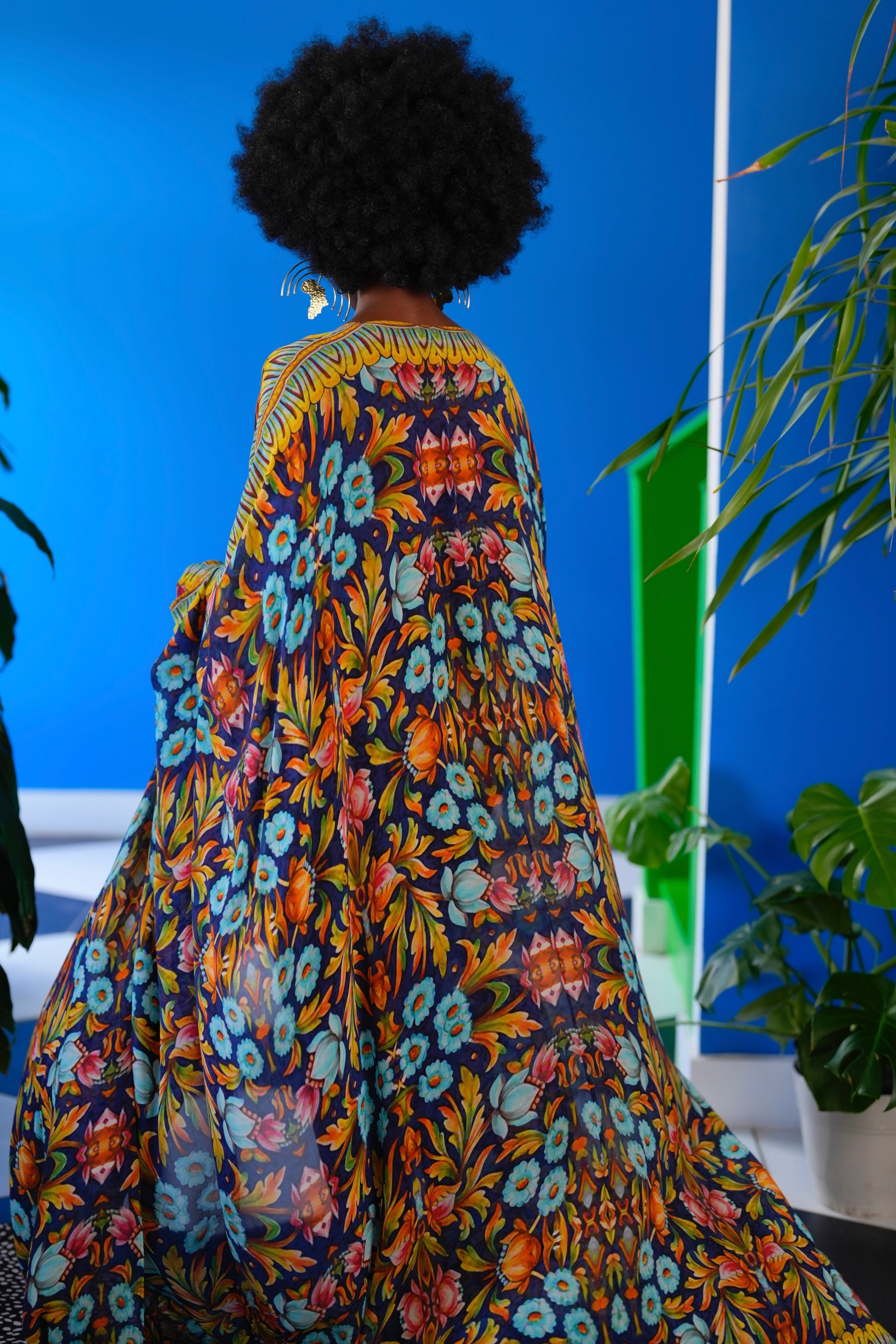 Person wearing a colorful floral dress with a blue wall and plants in the background