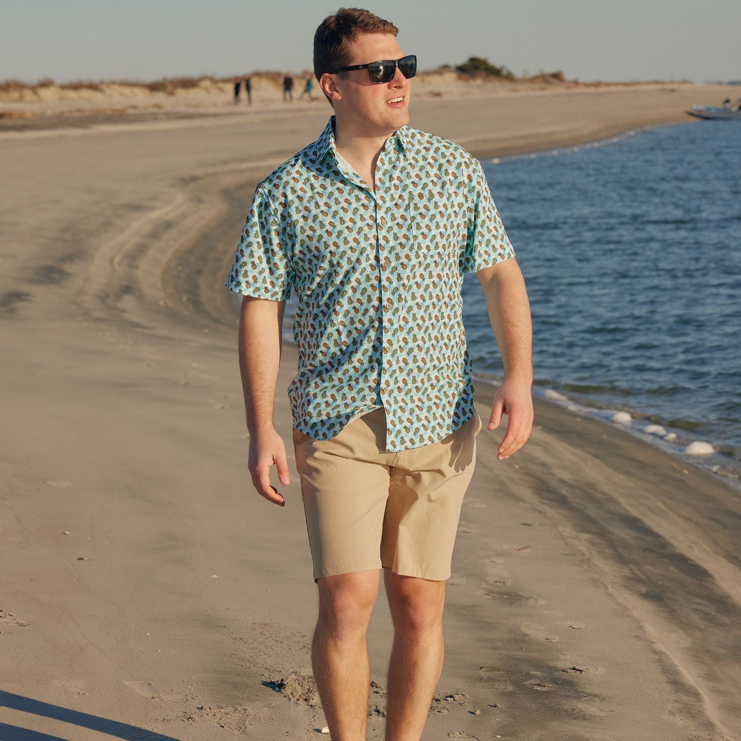 Man walking on a beach wearing a patterned shirt and sunglasses