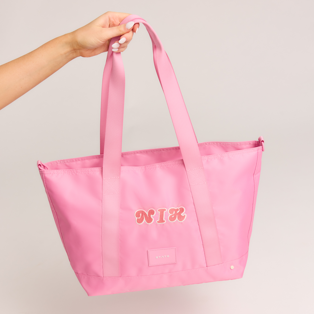 Pink tote bag with 'NIK' branding held by a hand against a plain background