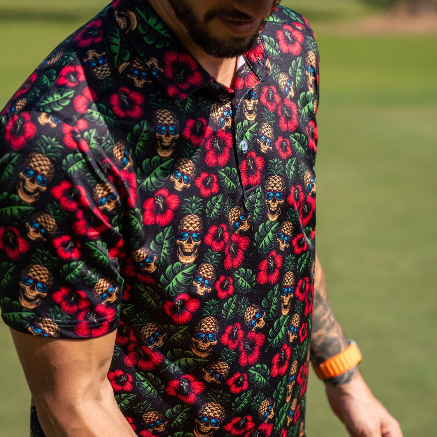 Person wearing a colorful patterned shirt with flowers and skulls on a grassy background