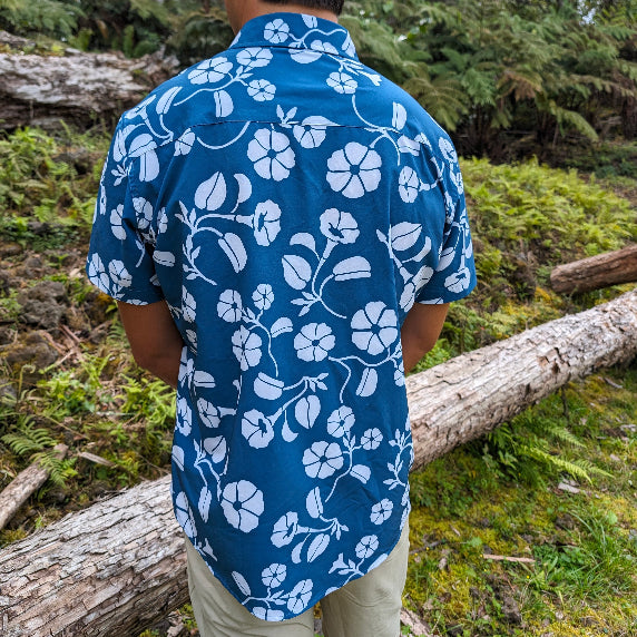 Person wearing a blue floral shirt standing in a forest setting