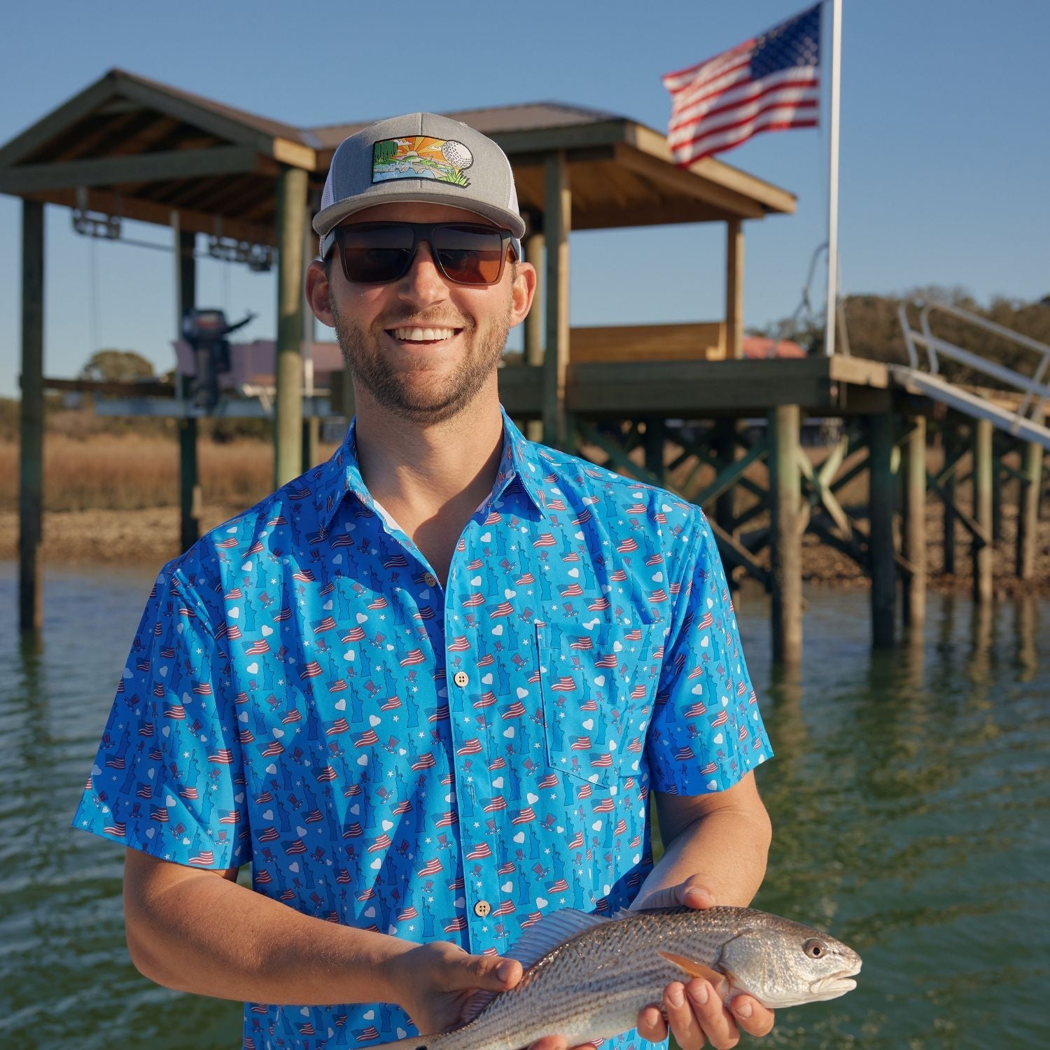 Man holding a fish by a dock with an American flag in the background