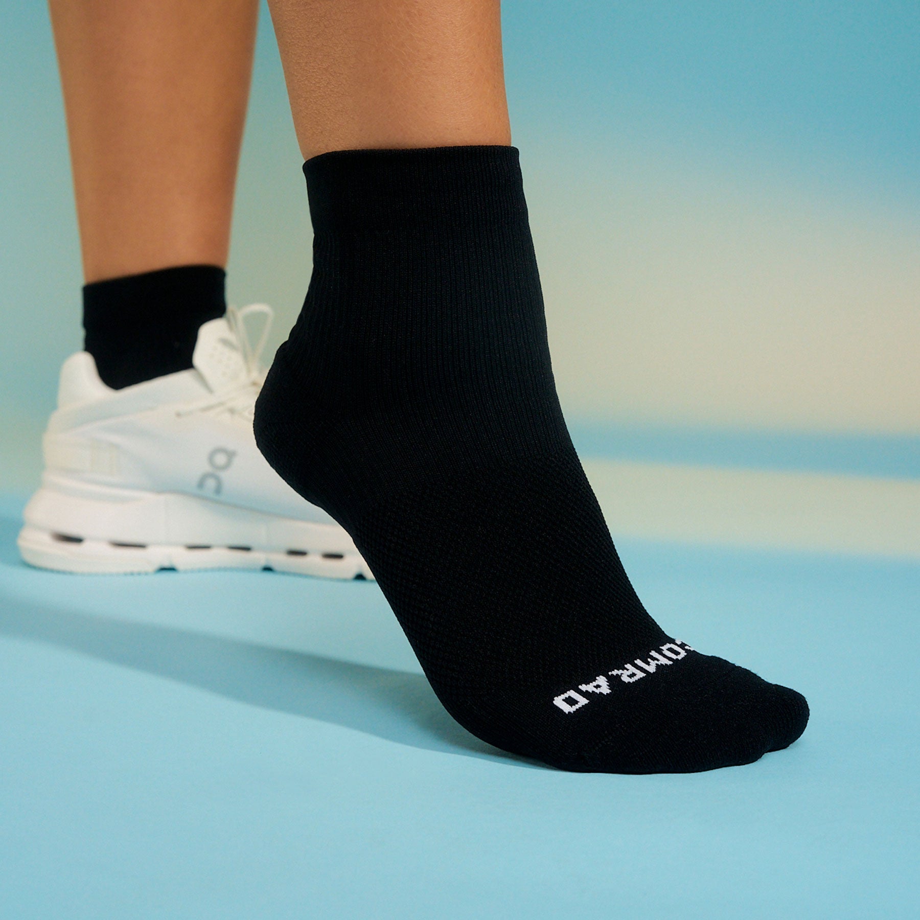 Black socks with a brand logo worn by a person on a blue background