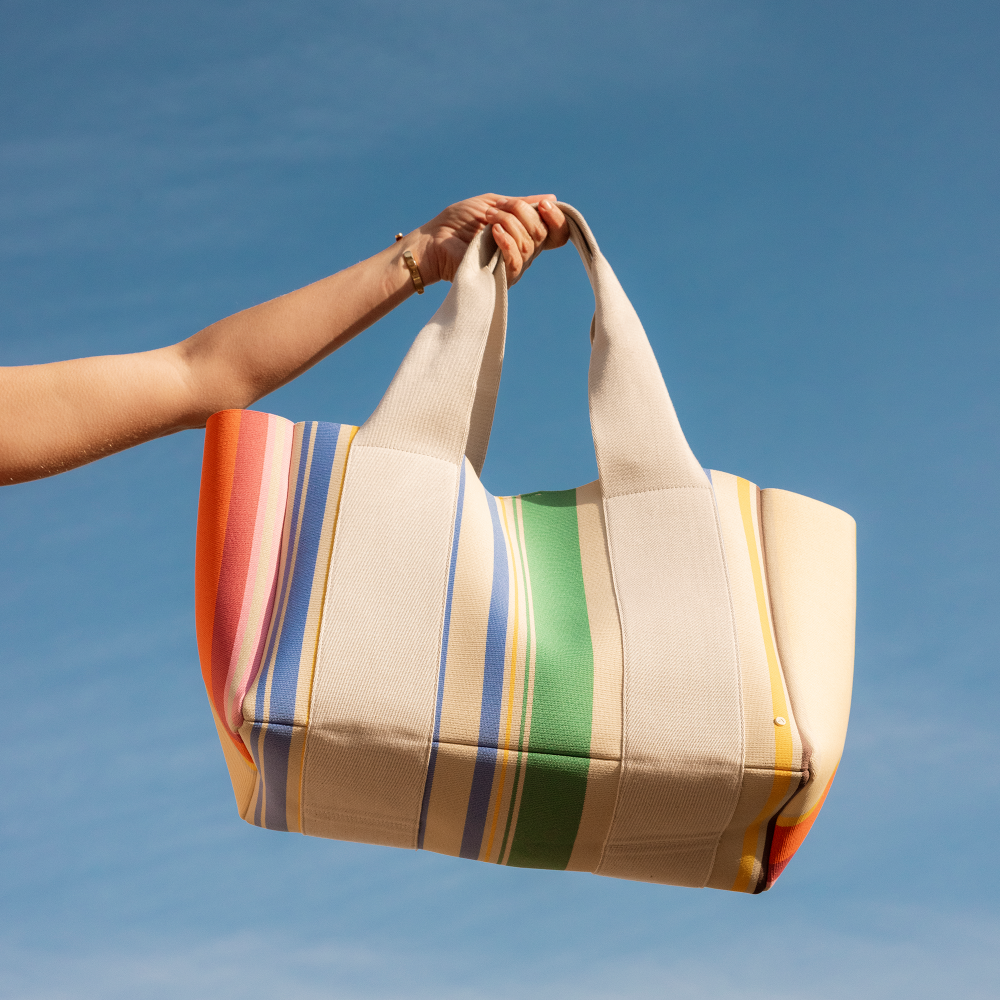 Colorful striped tote bag held against a blue sky