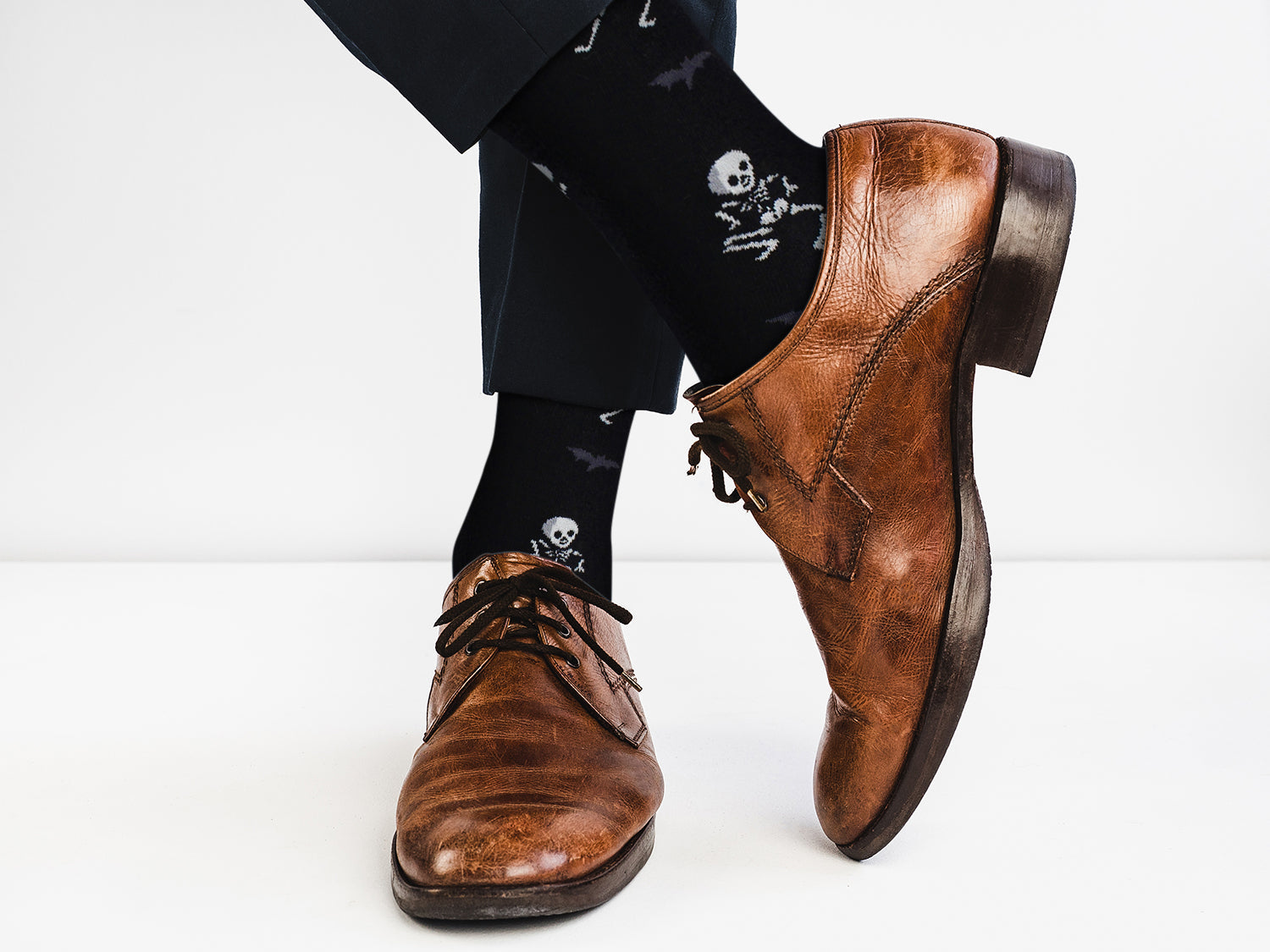 Brown leather shoes worn with black pants and socks featuring skull designs on a white background