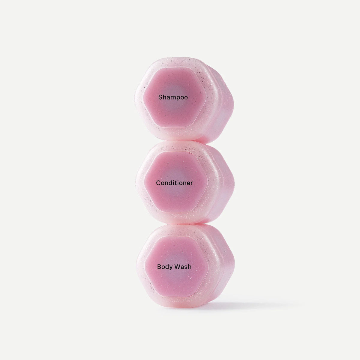 Three pink hexagonal toiletry containers stacked vertically on a light gray background, labeled Shampoo, Conditioner, and Body Wash.