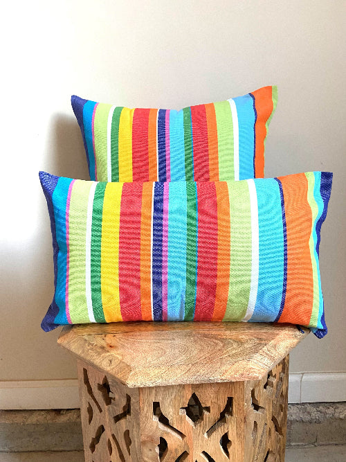 Two colorful striped pillows on a wooden stool against a neutral wall.