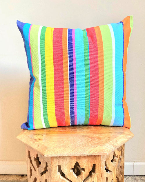 Colorful striped pillow on a wooden stool against a neutral wall