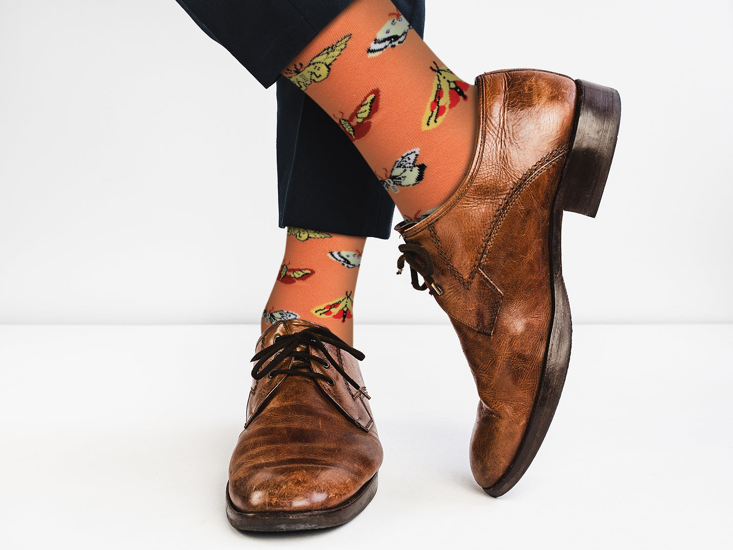 Brown leather shoes with a person wearing patterned socks on a white background