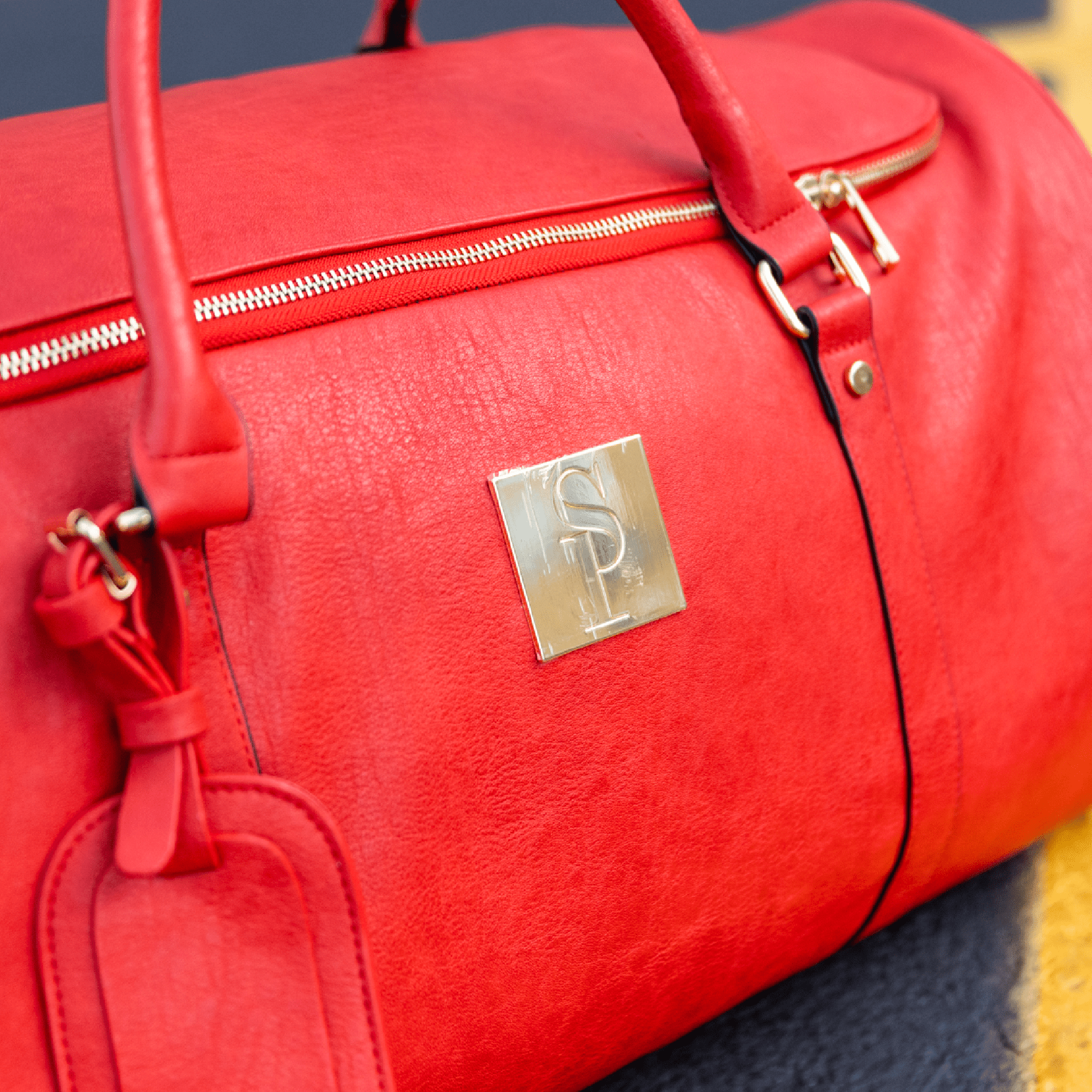 Red duffel bag with a gold logo on a dark surface